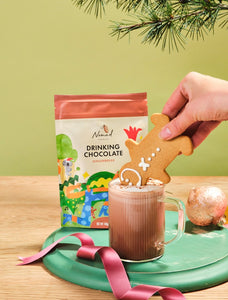 Nomad Drinking Chocolate Gingerbread bag with cup of hot chocolate. Gingerbread manning dunked into cup head first. Ribbon and Christmas bauble decoration.
