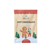 Load image into Gallery viewer, A stand-up pouch of NomadChocolate Hot Chocolate Gingerbread, featuring a beige background with a gingerbread man and woman illustration, green pine trees, and a coral-red top and bottom border.
