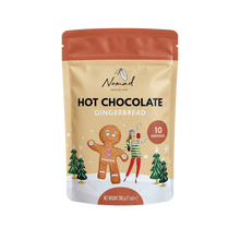 Load image into Gallery viewer, A stand-up pouch of Nomad Chocolates Hot Chocolate Gingerbread, featuring a warm beige background with festive illustrations of a gingerbread man, a woman in a holiday sweater, and Christmas trees. The pouch has a terracotta orange top and bottom band, and is shown on a clean white background.