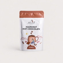 Load image into Gallery viewer, A 300g stand-up pouch of Nomad Chocolates Hazelnut Hot Chocolate, featuring a white bag with a copper-brown top, a central illustration of a hot chocolate mug, and black text on a clean, light off-white background.