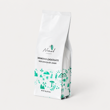 Load image into Gallery viewer, A white stand-up pouch of Nomad Chocolate Company drinking chocolate, West Africa 45% dark, featuring green botanical illustrations and black text, set against a clean white background.