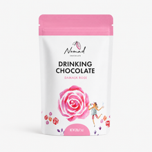 Load image into Gallery viewer, A stand-up pouch of Nomad Chocolate Drinking Chocolate in Damask Rose flavor. The packaging is white with a bright pink top band, featuring a large pink rose illustration, small floral accents, and a small dancing woman graphic on the front.