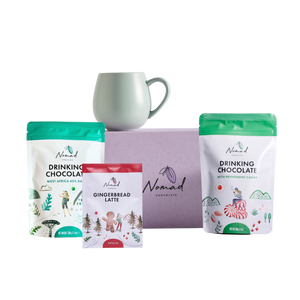 Nomad Drinking Chocolate packages with a mug on a white background. mage of Nomad chocolate gift box in lilac colour, Robert gordon mug , Nomad drinking chocolate west Africa 45% dark and nomad hot chocolate with peppermint candy 200g and gingerbread latte in the 40g bag  