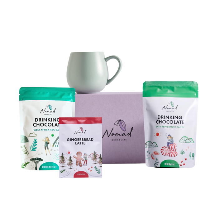 Nomad Drinking Chocolate packages with a mug on a white background. mage of Nomad chocolate gift box in lilac colour, Robert gordon mug , Nomad drinking chocolate west Africa 45% dark and nomad hot chocolate with peppermint candy 200g and gingerbread latte in the 40g bag  