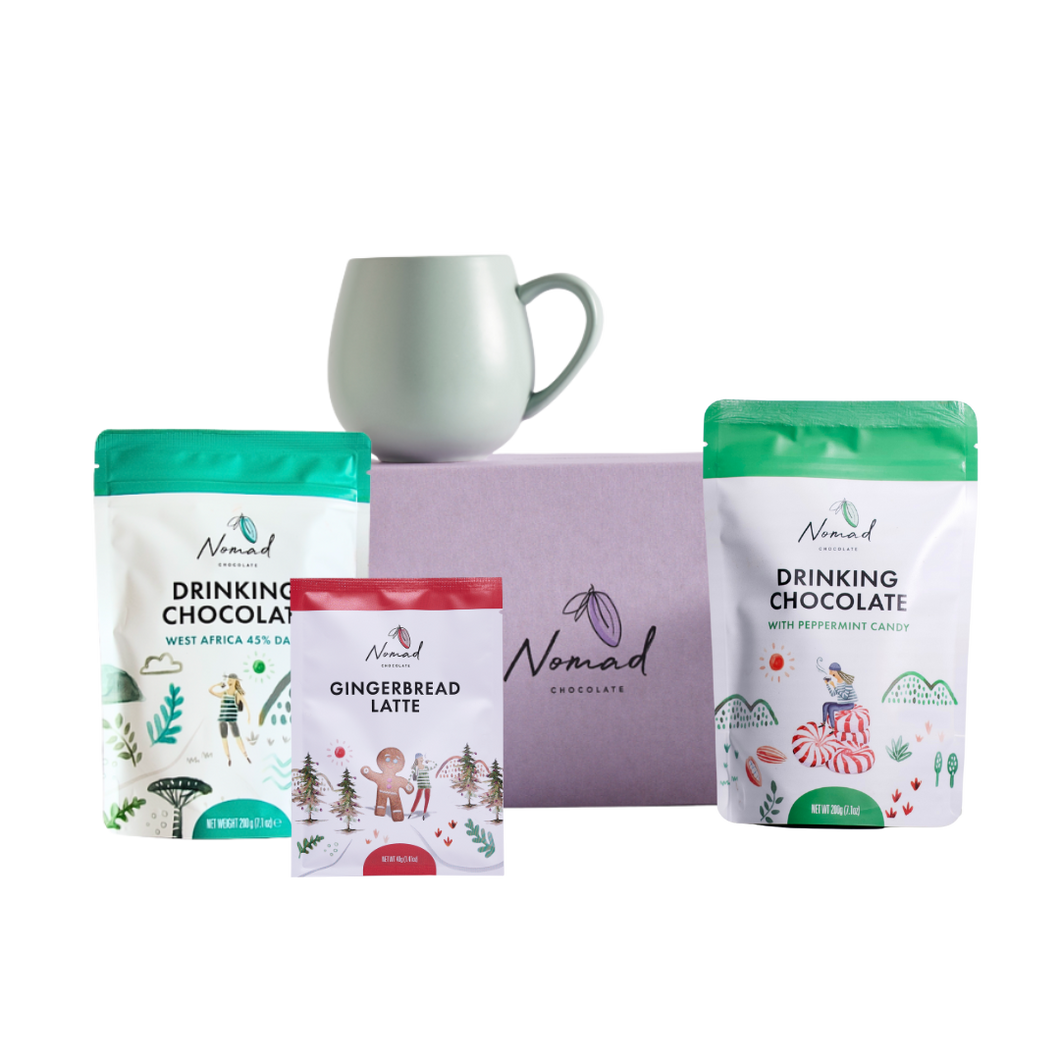 Nomad Drinking Chocolate packages with a mug on a white background. mage of Nomad chocolate gift box in lilac colour, Robert gordon mug , Nomad drinking chocolate west Africa 45% dark and nomad hot chocolate with peppermint candy 200g and gingerbread latte in the 40g bag  