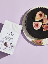Load image into Gallery viewer, Nomad Chocolate Vegan, dairy and gluten free 72% dark chocolate buttons baking chocolate. Lifestyle photo of Nomad Chocolate Button Bag next to a chocolate torte decorated with fig slices.