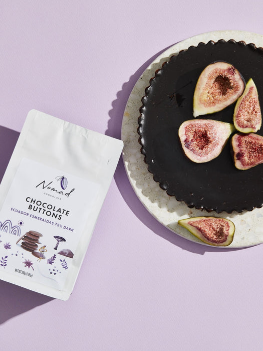 Nomad Chocolate Vegan, dairy and gluten free 72% dark chocolate buttons baking chocolate. Lifestyle photo of Nomad Chocolate Button Bag next to a chocolate torte decorated with fig slices.