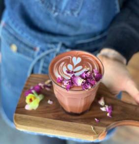 Barista holding a cafe style made hot Nomad Chocolate West Africa 45% Dark, decorated with edible flowers